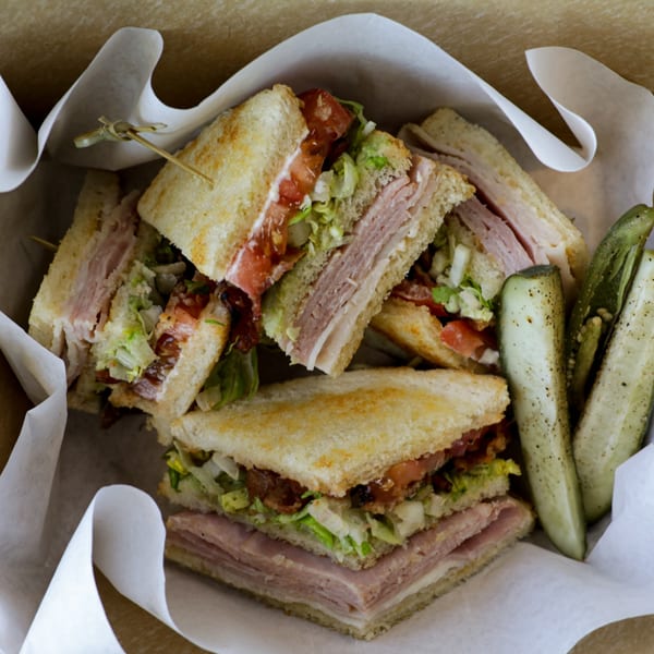 Club sandwiches with ham, turkey, bacon, lettuce, and tomato, served with pickle spears.