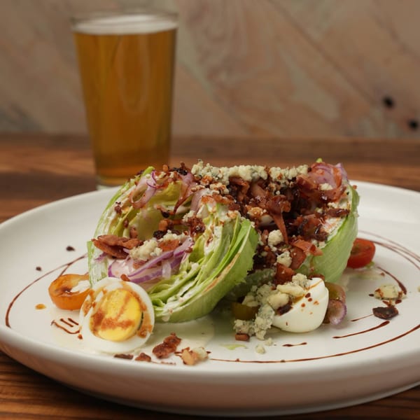 West Main Taproom's wedge salad with bacon, blue cheese, egg, and tomatoes, with a beer in the background.