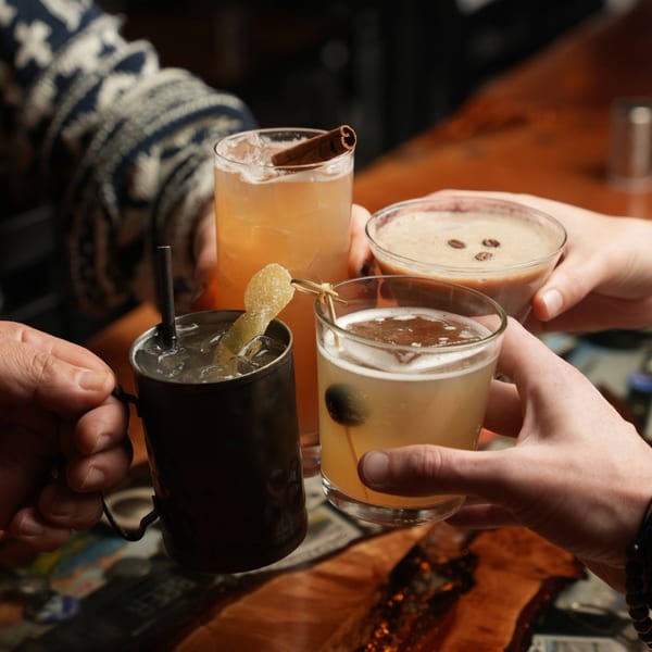 Four hands holding different cocktails, including a Moscow Mule, an espresso martini, and two other drinks.