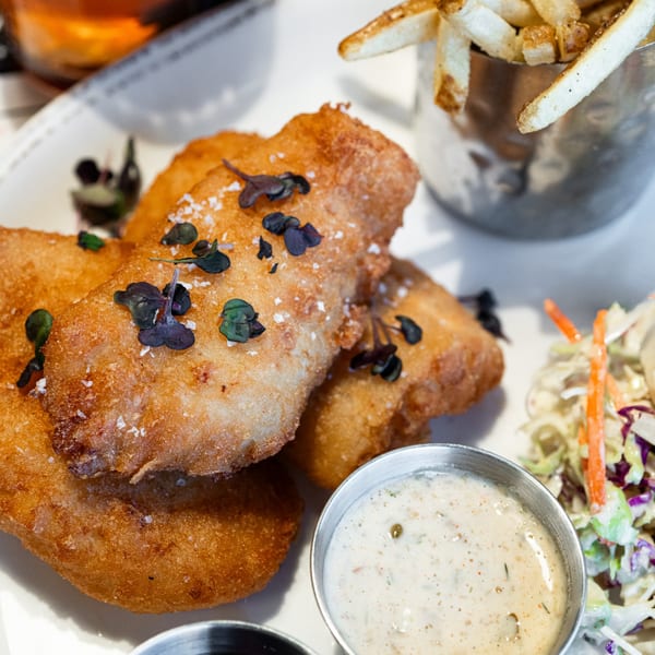 Golden-brown fish and chips with tartar sauce, coleslaw, and a side of fries at West Main Taproom.