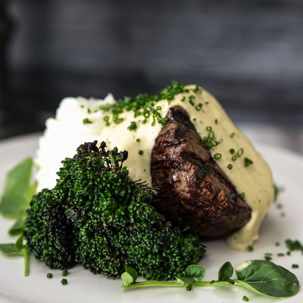 Grilled steak with creamy sauce, mashed potatoes, and roasted broccoli on a white plate.